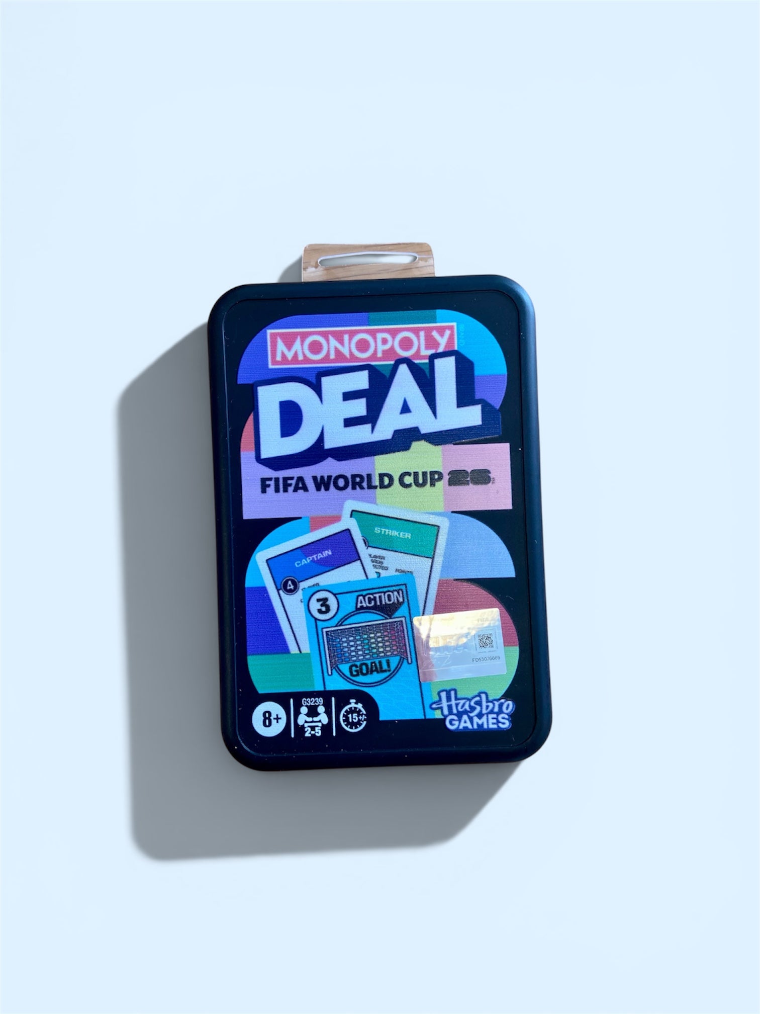 FIFA World Cup 2022 Monopoly Deal board game in a dark blue metal tin with a clear plastic handle, shown on a light blue background with a soft shadow.